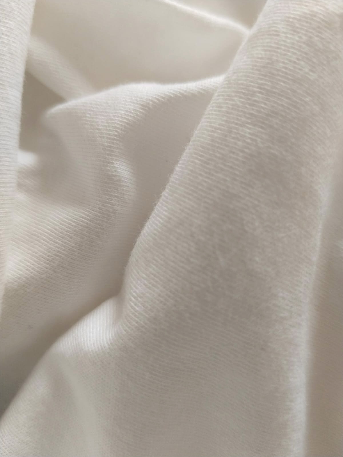 Macro photograph of CRW 25s combed 100% cotton single jersey in optical white — knitted loop structure and surface